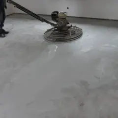 Pracownik poleruje betonową posadzkę maszyną. Powierzchnia jest gładka i jednolita, tworząc nowoczesny **beton polerowany**.