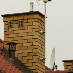 Ceglanego komina z dwoma kratkami wentylacyjnymi, które mogą służyć jako odpowietrzenie kanalizacji. Na dachu widać antenę satelitarną.