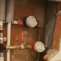 Instalacja wodna z dwoma licznikami i czerwonym zaworem.