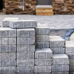Stosy szarych kostek brukowych, gotowych do ułożenia. Różne rodzaje kostki brukowej czekają na stworzenie pięknego podjazdu.