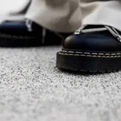 Czarne buty na grubej podeszwie stoją na kamiennym dywanie. Wady i zalety takiego wykończenia podłoża są widoczne w detalu.