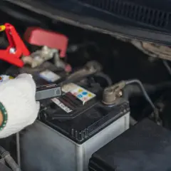 Rękawica w białej rękawiczce trzyma kabel z klemami, pokazując, jak podłączyć akumulator.