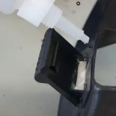 Kropla cyjanoakrylu z butelki precyzyjnie aplikowana na czarny plastikowy element, naprawiając go.