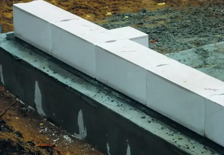 Białe bloczki z betonu komórkowego, prawdopodobnie do budowy fundamentów, leżą na warstwie izolacji. Nivoplan zapewnia stabilność konstrukcji.