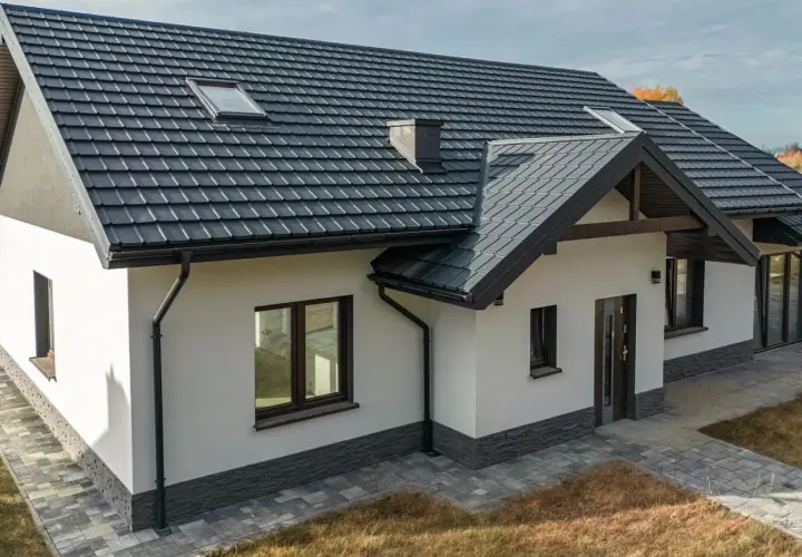Nowoczesny dom z ciemnym dachem i solidnymi systemami rynnowymi, chroniącymi jego fundamenty.