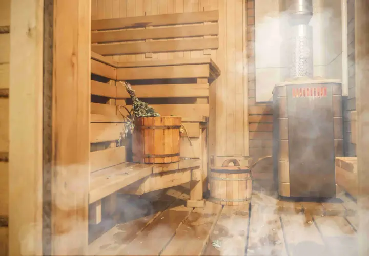 Drewniana sauna z piecem i wiaderkiem z miotełką. Idealne miejsce, by poczuć ciepło i relaks, jakbyś sam wiedział, jak zbudować saunę.