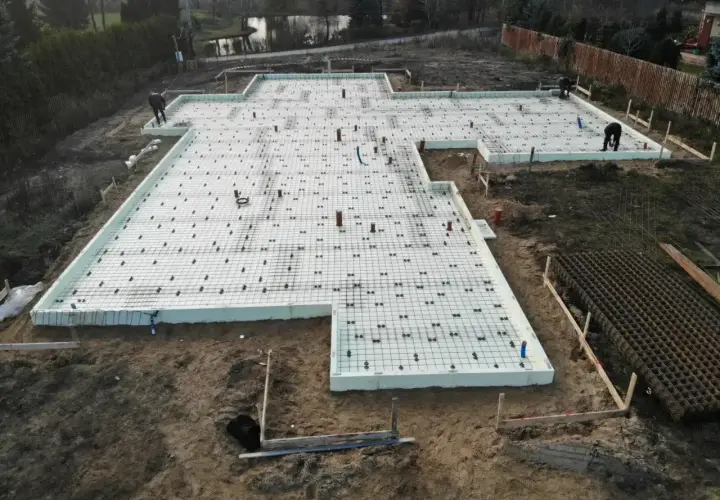 Fundament pod budowę z siatką zbrojeniową i rurami. Szybki beton zostanie wkrótce wylany na tę przygotowaną powierzchnię.