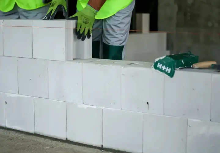Budowa ściany z białych pustaków silikatowych. Ręce w zielonych rękawicach układają kolejny blok.