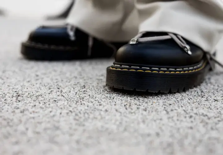 Czarne buty na grubej podeszwie stoją na kamiennym dywanie. Wady i zalety takiego wykończenia podłoża są widoczne w detalu.