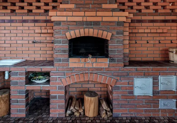 Solidny, murowany prosty grill z cegły, gotowy na letnie przyjęcia. Obok zlew i drewniana beczka.
