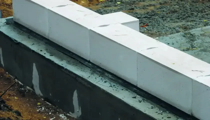 Białe bloczki z betonu komórkowego, prawdopodobnie do budowy fundamentów, leżą na warstwie izolacji. Nivoplan zapewnia stabilność konstrukcji.