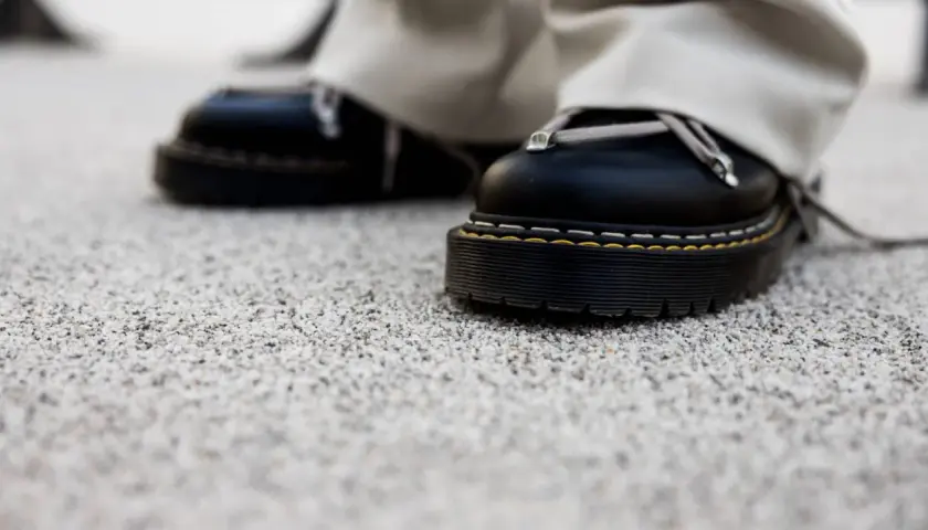 Czarne buty na grubej podeszwie stoją na kamiennym dywanie. Wady i zalety takiego wykończenia podłoża są widoczne w detalu.
