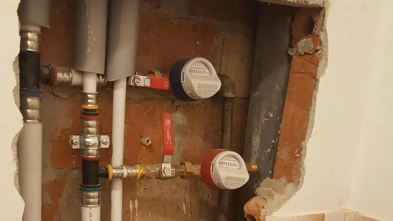 Instalacja wodna z dwoma licznikami i czerwonym zaworem.