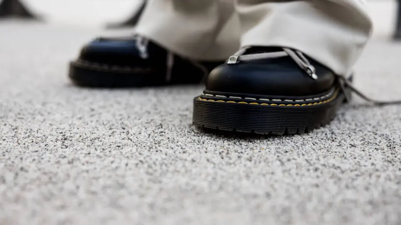 Czarne buty na grubej podeszwie stoją na kamiennym dywanie. Wady i zalety takiego wykończenia podłoża są widoczne w detalu.
