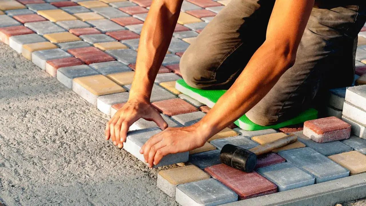 Układanie kostki brukowej na betonie. Ręce pracownika precyzyjnie dopasowują kolejne elementy, tworząc wzór z kolorowych kostek.