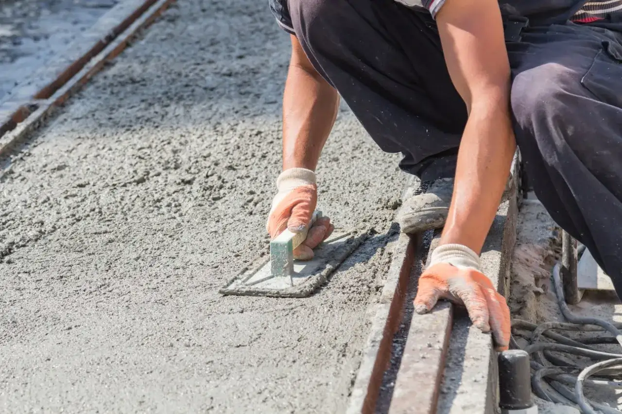 Pracownik wygładza świeży beton, dbając o właściwe suchy beton proporcje. Ręce w rękawiczkach trzymają kielnię.