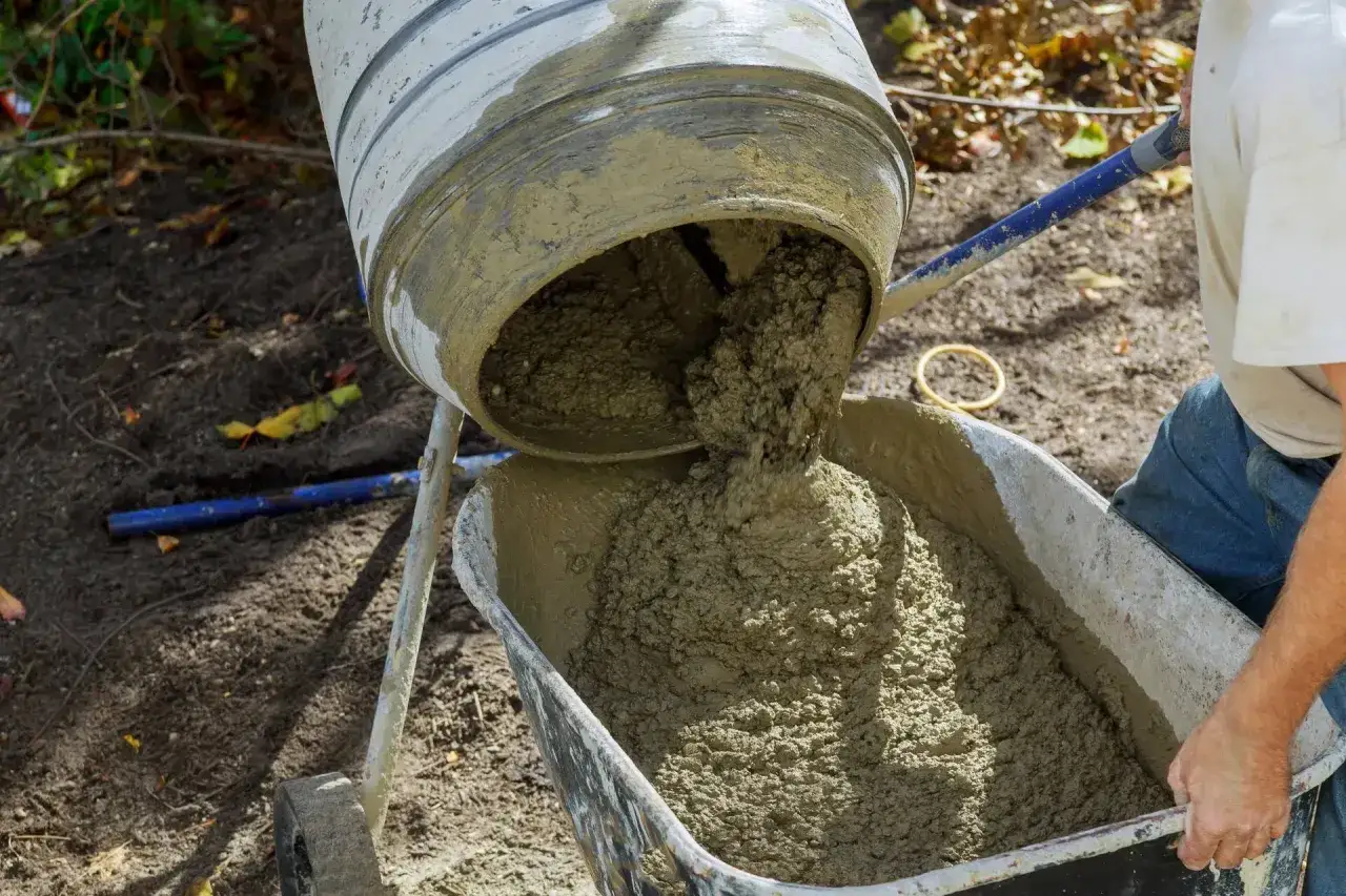 Mieszanka betonu wylewa się z betoniarki do taczki. Trudno określić, ile piasku na worek cementu, ale efekt jest widoczny.